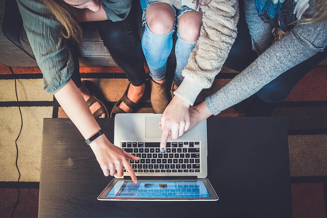 Group of students gathered around a laptop, pointing at the screen