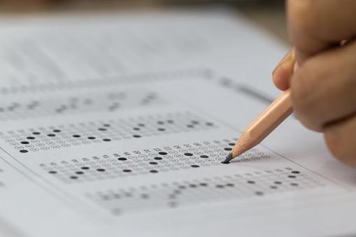 A hand holding a pencil filling in an exam bubble answer sheet. en español: Una mano sosteniendo un lápiz rellenando la hoja de respuestas de un examen.