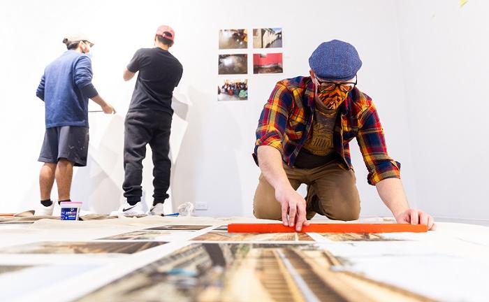 Andrew Cline working on installation with people in the background hanging art.