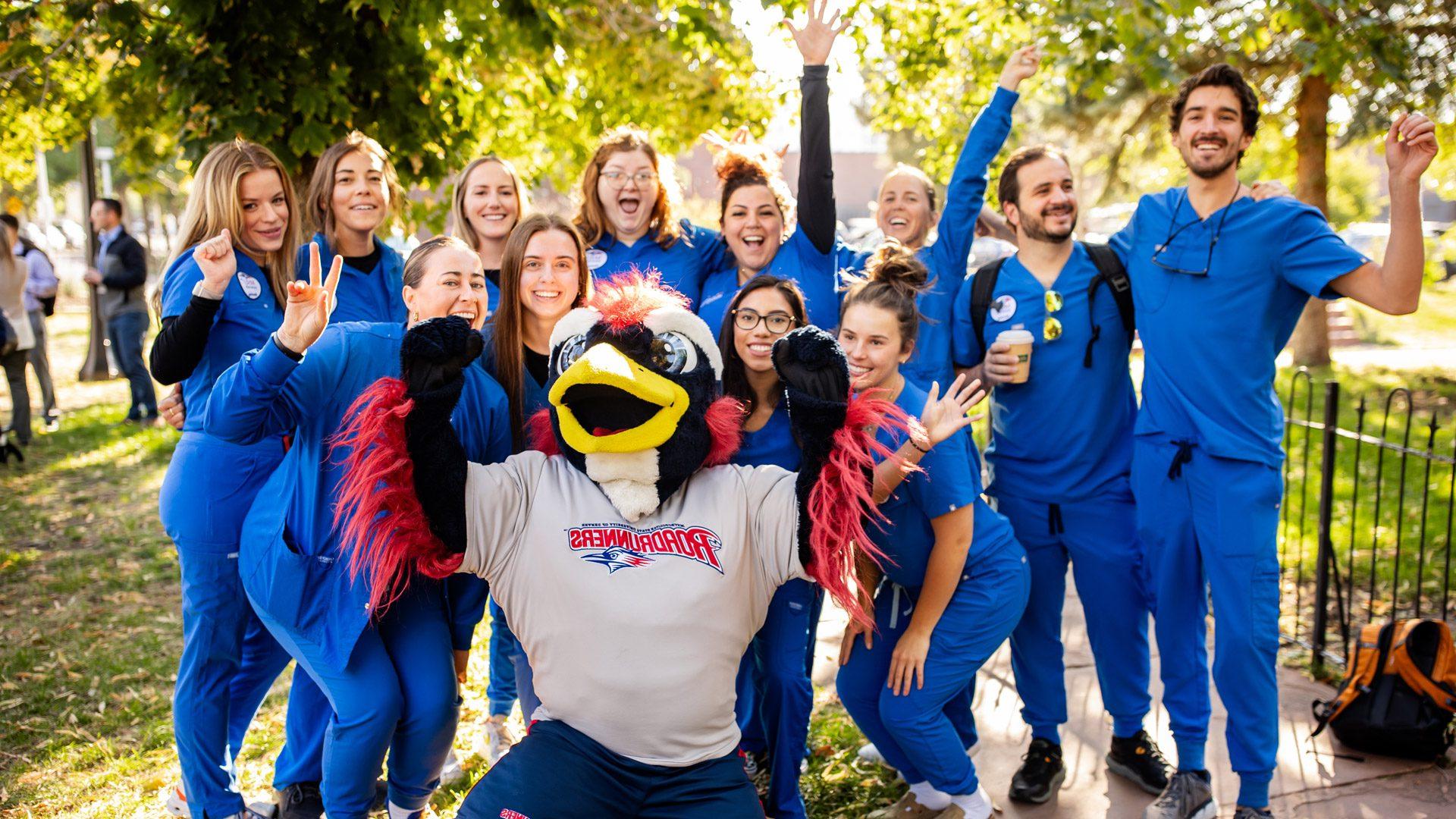 A group of nursing students wearing their scrubs posing for a photo with Rowdy in the 9th Street Park at the Health Institute groundbreaking ceremony.