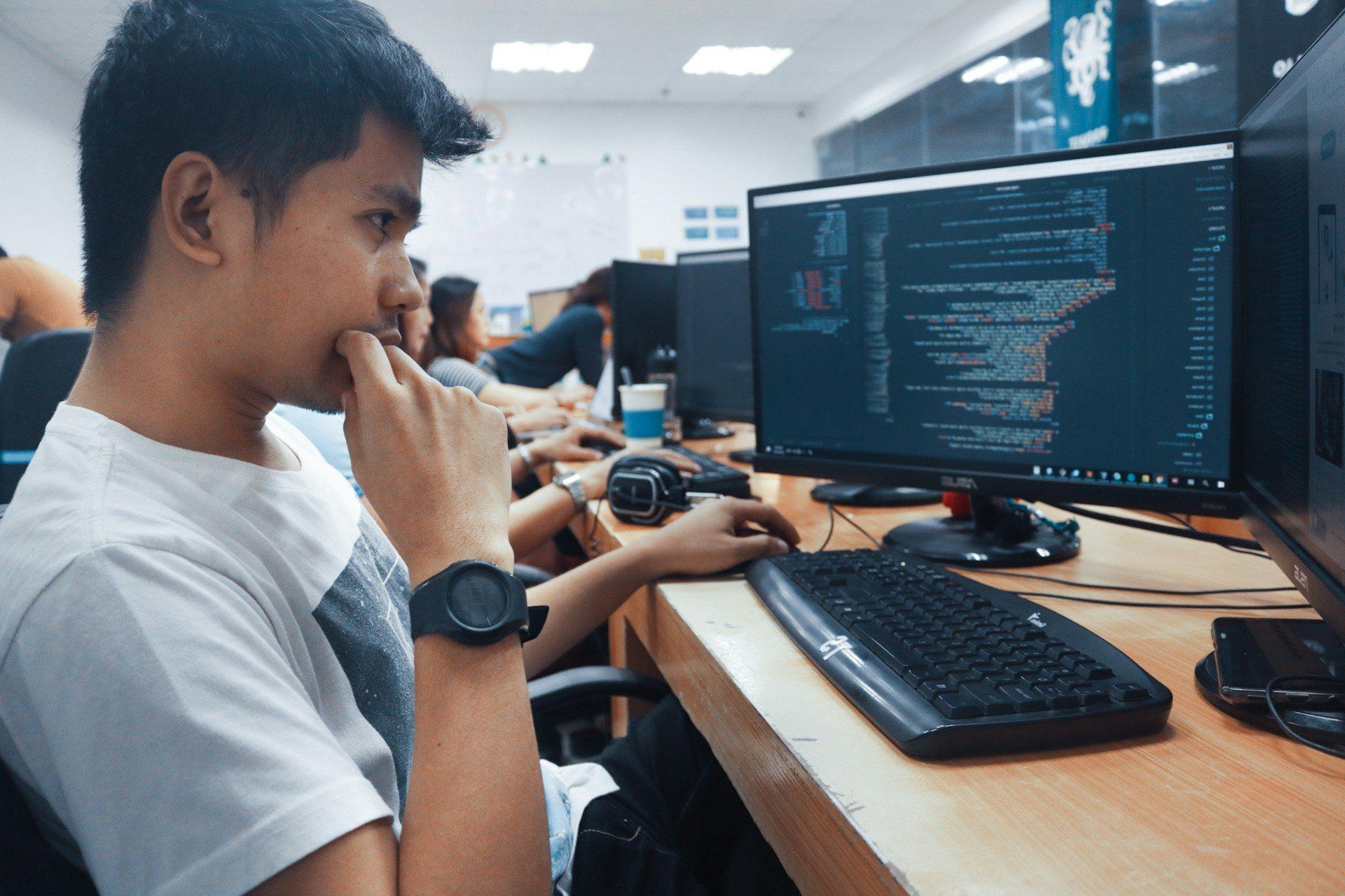 A student in a classroom reviewing work on a computer monitor.